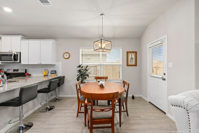 dining area with vaulted ceiling, light wood-style flooring, visible vents, and baseboards