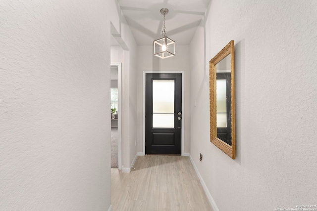 doorway to outside featuring a textured wall, light wood-style flooring, and baseboards