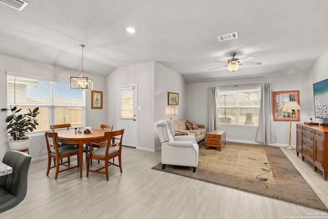 dining room with vaulted ceiling, light wood-style flooring, a textured ceiling, and visible vents