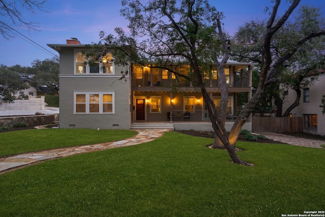 back of property featuring a balcony, a chimney, crawl space, a yard, and stucco siding