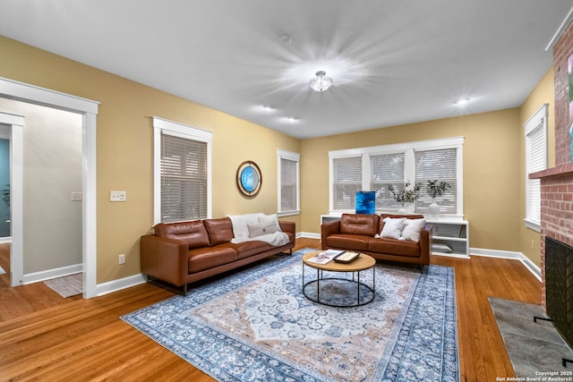 living room with a brick fireplace, baseboards, and wood finished floors