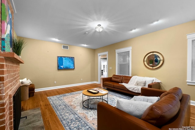 living area featuring baseboards, a fireplace, visible vents, and wood finished floors