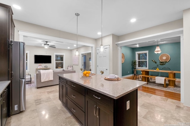 kitchen featuring decorative light fixtures, freestanding refrigerator, open floor plan, a kitchen island, and dark brown cabinets