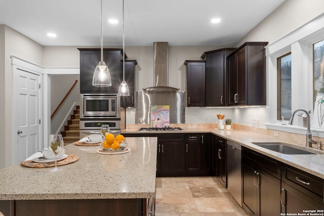 kitchen with light stone counters, decorative light fixtures, stainless steel appliances, a sink, and wall chimney exhaust hood