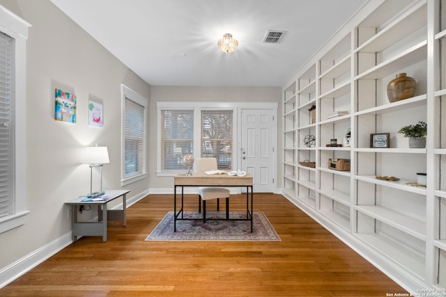 office space featuring built in features, baseboards, visible vents, and wood finished floors