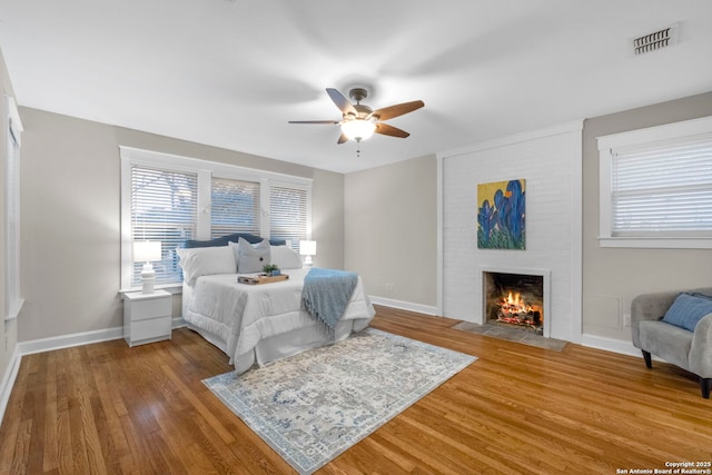 bedroom featuring a brick fireplace, visible vents, baseboards, and wood finished floors