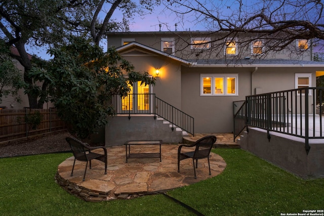 back of property at dusk with stucco siding, a lawn, stairway, a patio area, and fence