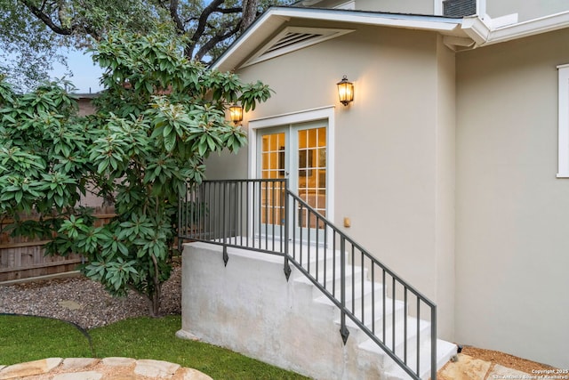 entrance to property featuring french doors, fence, and stucco siding