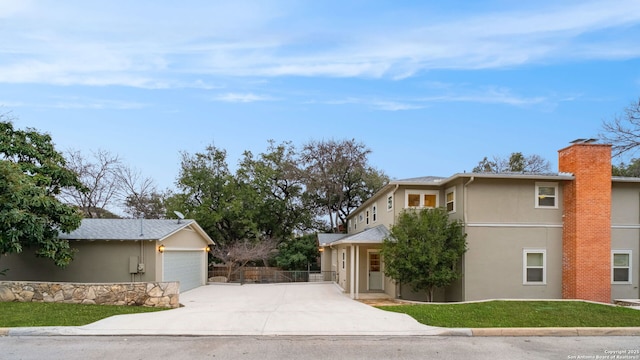 view of front facade featuring a chimney, stucco siding, concrete driveway, fence, and a garage