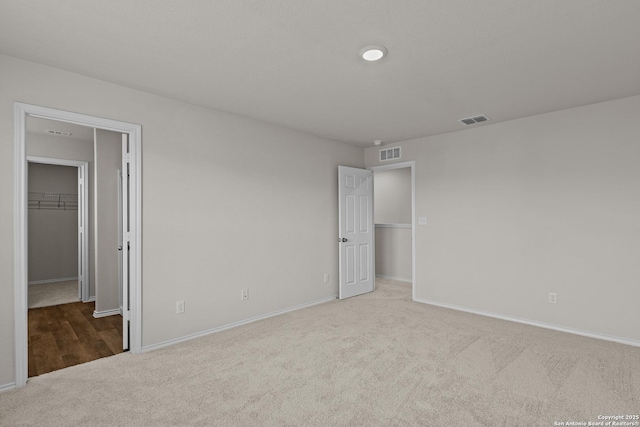 unfurnished bedroom with light carpet, a spacious closet, a closet, and visible vents