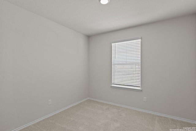 spare room featuring light carpet and baseboards