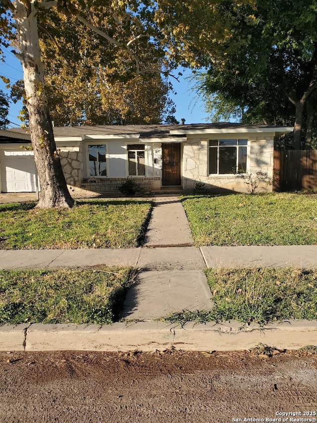 view of front of home featuring a front yard, stone siding, and an attached garage