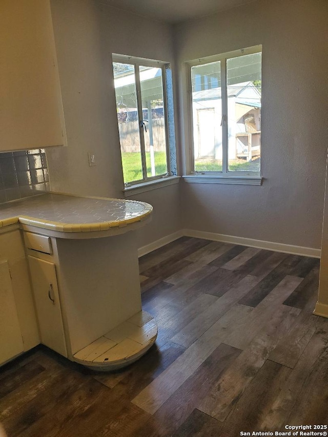 kitchen featuring a peninsula, dark wood-style floors, baseboards, and tile counters