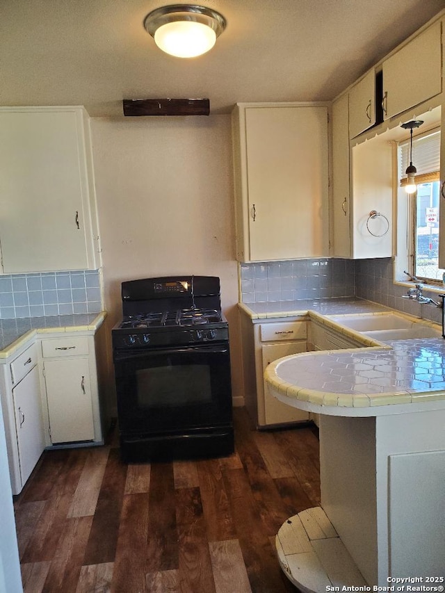 kitchen with tile countertops, a sink, black range with gas stovetop, white cabinetry, and backsplash