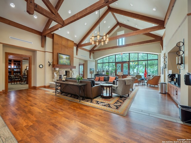 living area featuring a chandelier, high vaulted ceiling, a stone fireplace, light wood-type flooring, and beam ceiling