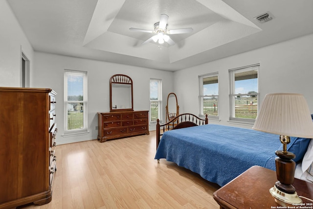 bedroom featuring light wood-style floors, a raised ceiling, visible vents, and ceiling fan