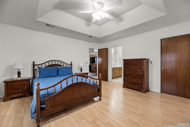 bedroom featuring light wood finished floors, ceiling fan, a tray ceiling, and visible vents