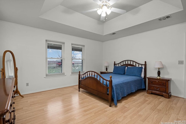 bedroom featuring light wood-style floors, baseboards, visible vents, and a raised ceiling