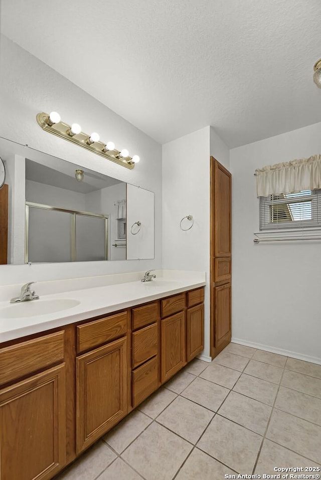 bathroom with double vanity, tile patterned floors, a textured ceiling, a shower stall, and a sink