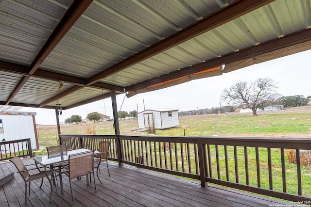 deck with an outbuilding, outdoor dining area, a rural view, a yard, and a shed