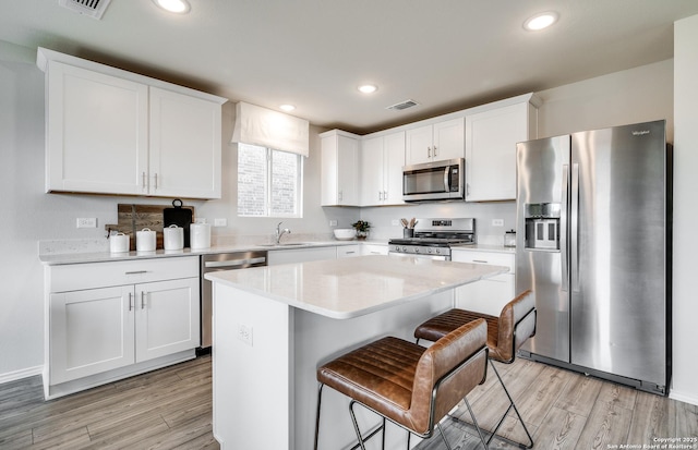 kitchen featuring stainless steel appliances, white cabinets, a kitchen island, and a sink