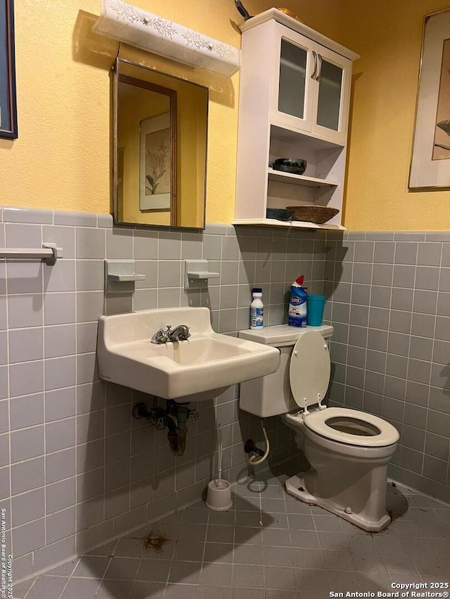 bathroom with a wainscoted wall, tile walls, toilet, a sink, and tile patterned floors