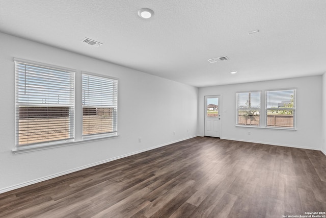 unfurnished room with dark wood-style floors, baseboards, visible vents, and a textured ceiling