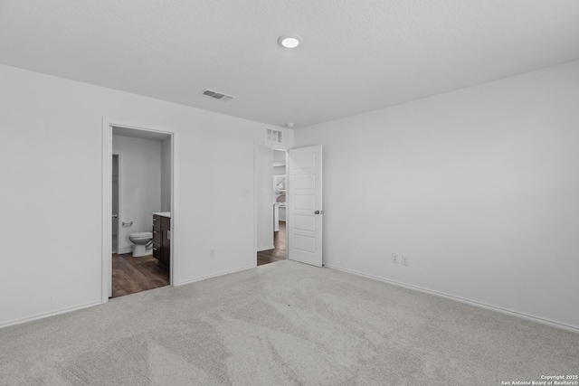 unfurnished bedroom featuring dark colored carpet, connected bathroom, visible vents, and baseboards