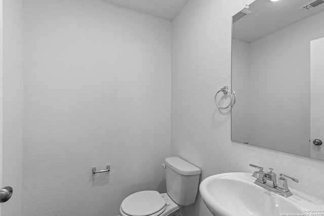 bathroom with a textured wall, visible vents, a sink, and toilet