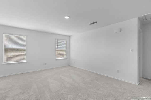 spare room featuring a textured ceiling, visible vents, a wealth of natural light, and light colored carpet