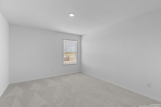 empty room featuring light carpet, a textured ceiling, and baseboards