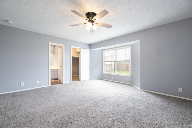 unfurnished bedroom featuring carpet floors, a walk in closet, a textured ceiling, and baseboards