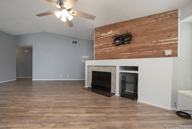 unfurnished living room with visible vents, a tiled fireplace, vaulted ceiling, a textured ceiling, and wood finished floors