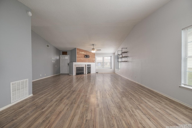 unfurnished living room featuring a tile fireplace, visible vents, ceiling fan, and wood finished floors