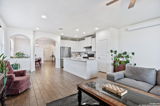 living area featuring a ceiling fan, visible vents, recessed lighting, arched walkways, and light wood-style floors