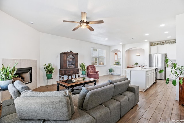 living room featuring recessed lighting, arched walkways, ceiling fan, light wood-style floors, and a tiled fireplace