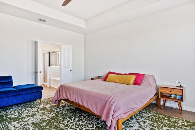 bedroom featuring visible vents, baseboards, ensuite bathroom, wood finished floors, and a ceiling fan