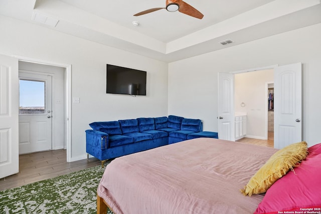 bedroom with visible vents, a ceiling fan, wood finished floors, baseboards, and a raised ceiling