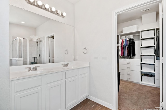 full bathroom with visible vents, double vanity, a sink, a shower stall, and a walk in closet