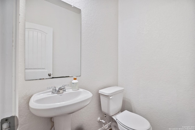 bathroom featuring toilet, a textured wall, and a sink