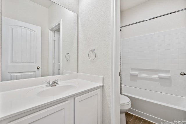 full bath featuring vanity, wood finished floors, shower / tub combination, toilet, and a textured wall