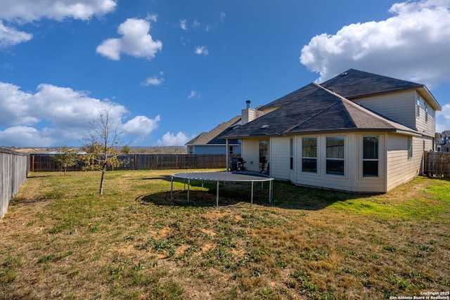 back of property with a fenced backyard, a lawn, a chimney, and a trampoline