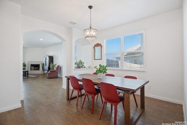 dining space featuring wood finished floors, visible vents, baseboards, an inviting chandelier, and a tile fireplace