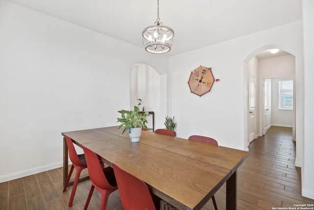 dining room featuring a notable chandelier, wood finished floors, arched walkways, and baseboards