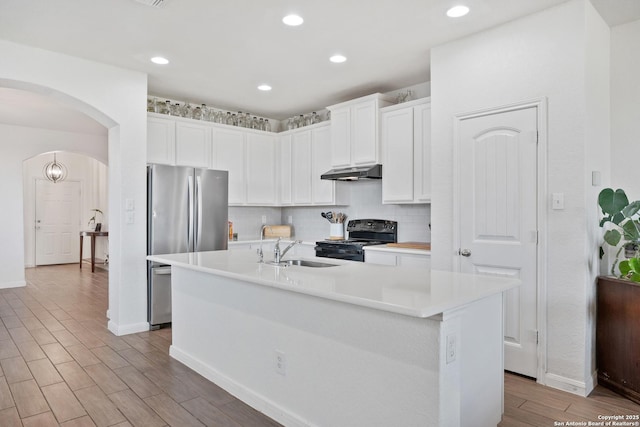 kitchen with electric range, a sink, under cabinet range hood, freestanding refrigerator, and arched walkways