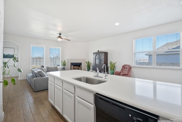 kitchen featuring a tiled fireplace, a sink, wood finished floors, white cabinets, and dishwasher