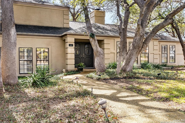 entrance to property featuring a shingled roof, a chimney, and stucco siding