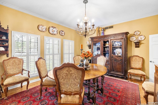 dining space featuring baseboards, visible vents, wood finished floors, an inviting chandelier, and crown molding