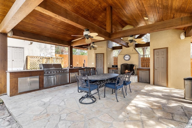 view of patio / terrace featuring a large fireplace, an outdoor kitchen, ceiling fan, a grill, and fence