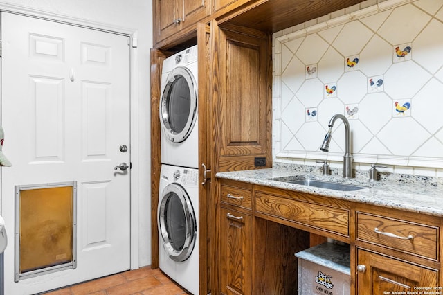 clothes washing area with stacked washing maching and dryer, laundry area, and a sink